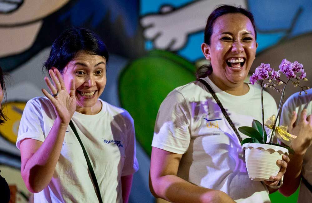 Two women are standing next to each other and smiling while holding potted flowers.