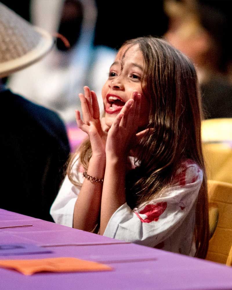 A little girl sitting at a table with her hands on her face