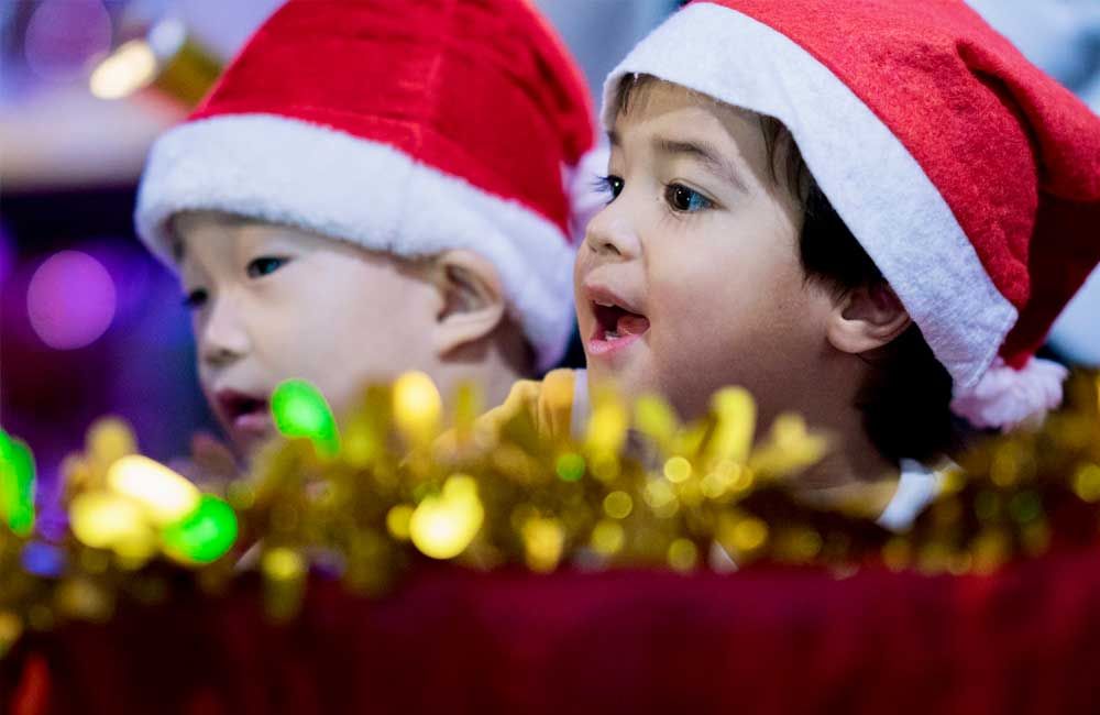 Two young boys wearing santa hats are standing next to each other.
