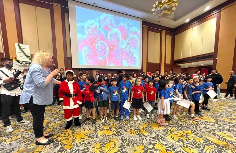 A woman is standing in front of a group of children dressed as santa claus.