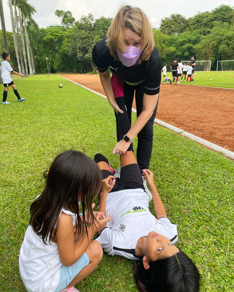 A woman wearing a mask is helping a young boy laying on the grass.