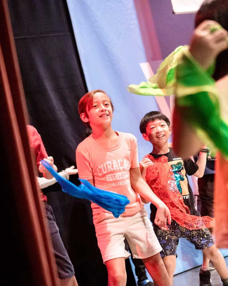 A group of children are dancing on a stage and one of them is wearing a shirt that says curaçao
