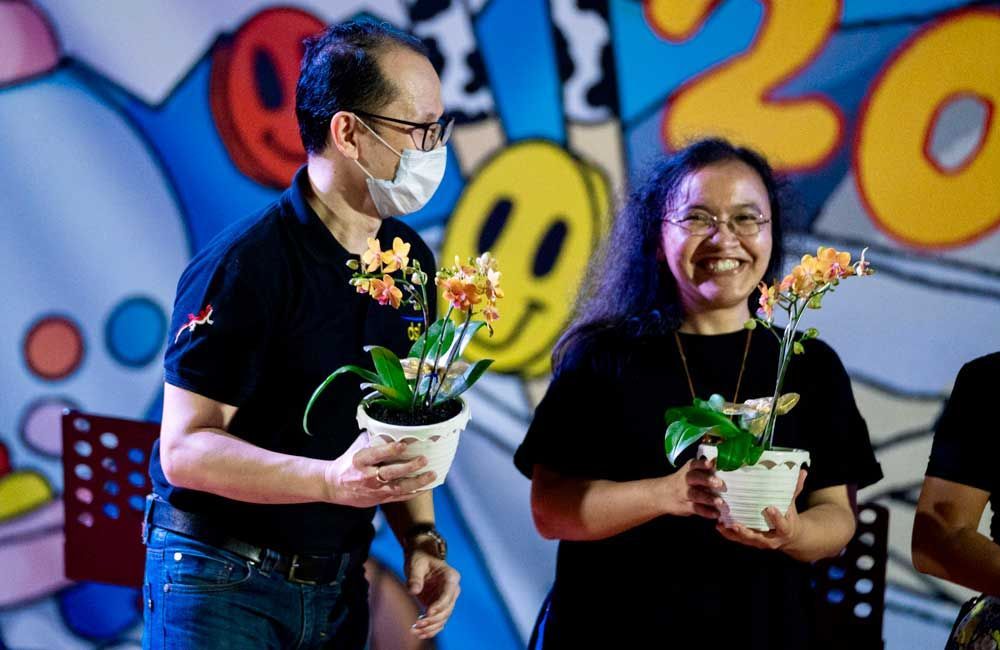 A man and a woman are holding potted flowers in front of a mural.
