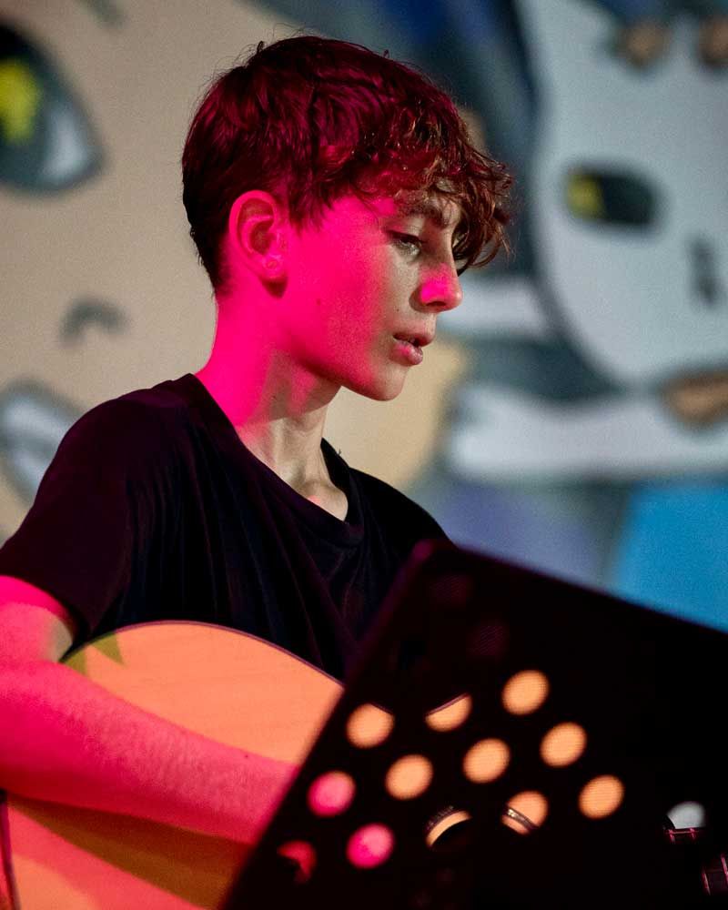 A young boy is playing a guitar in front of a graffiti wall