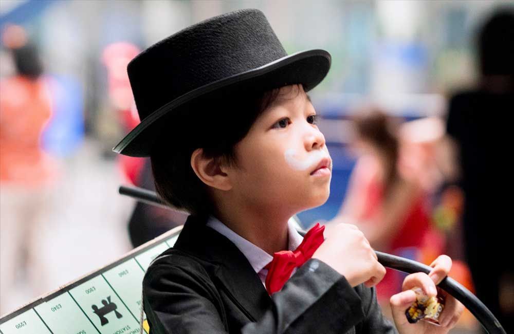 A young boy in a suit and top hat is holding a monopoly board.