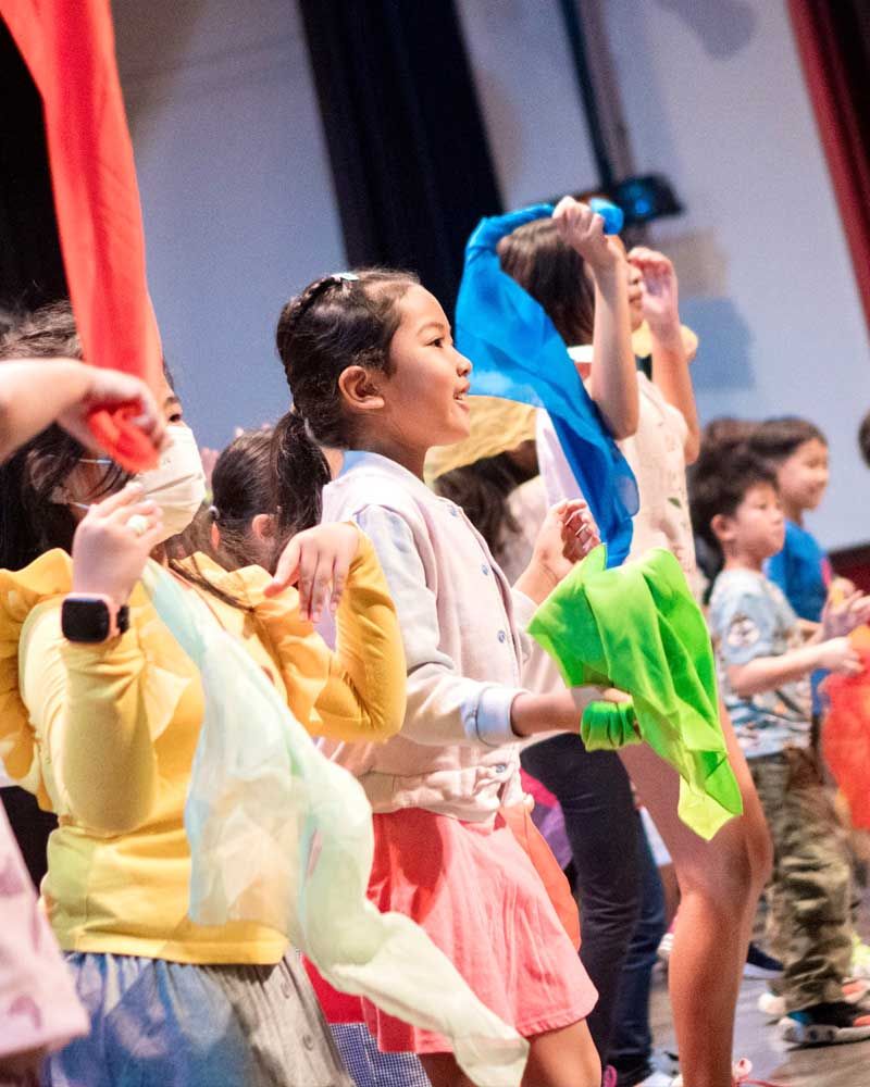 A group of children are standing on a stage holding flags.