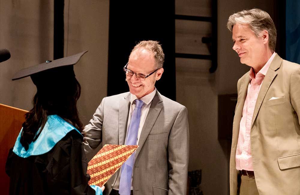 A man in a suit is shaking hands with a woman in a graduation cap and gown.