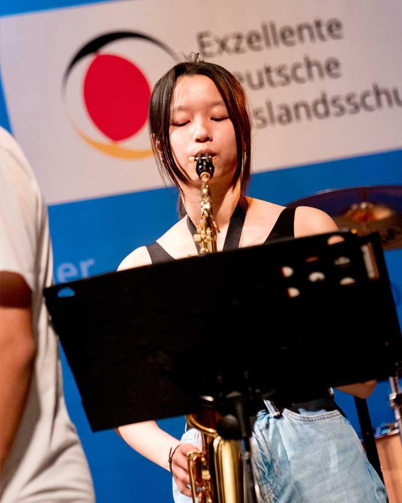 A woman playing a saxophone in front of a sign that says excellente