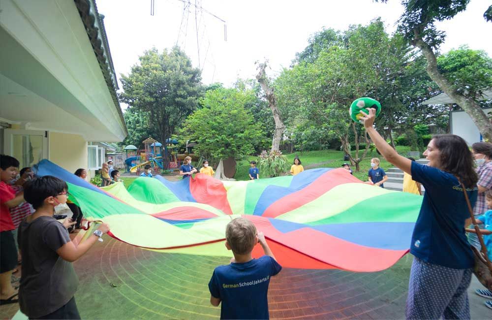 A group of children are playing with a colorful parachute.