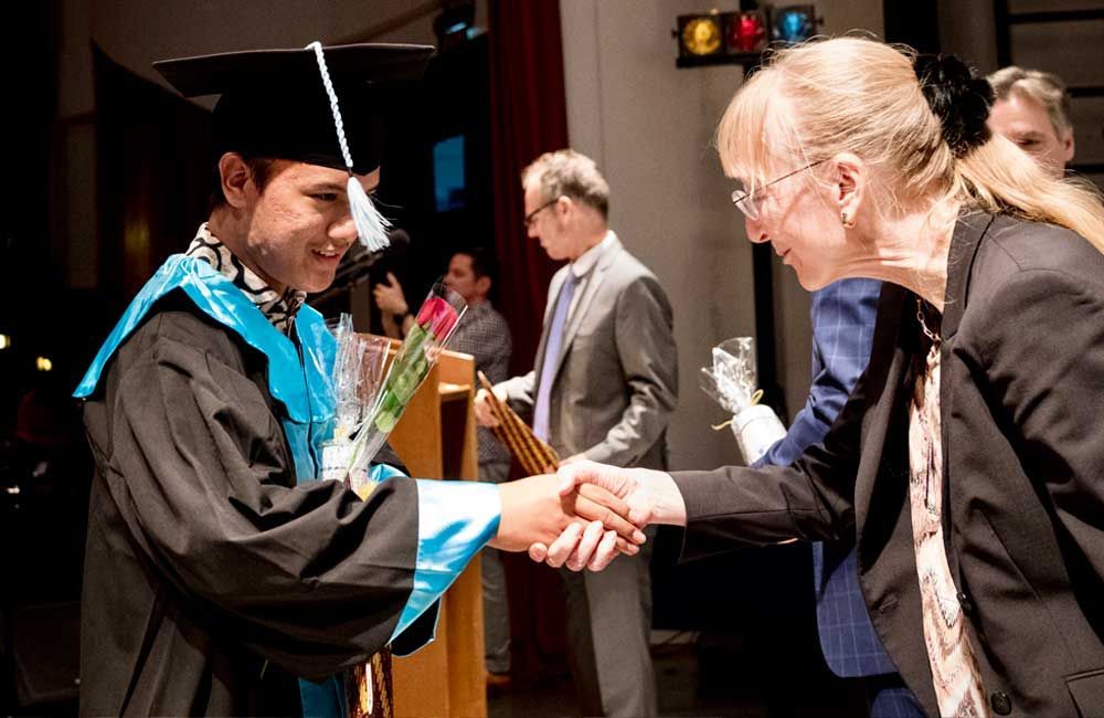 A man in a graduation cap and gown shakes hands with a woman