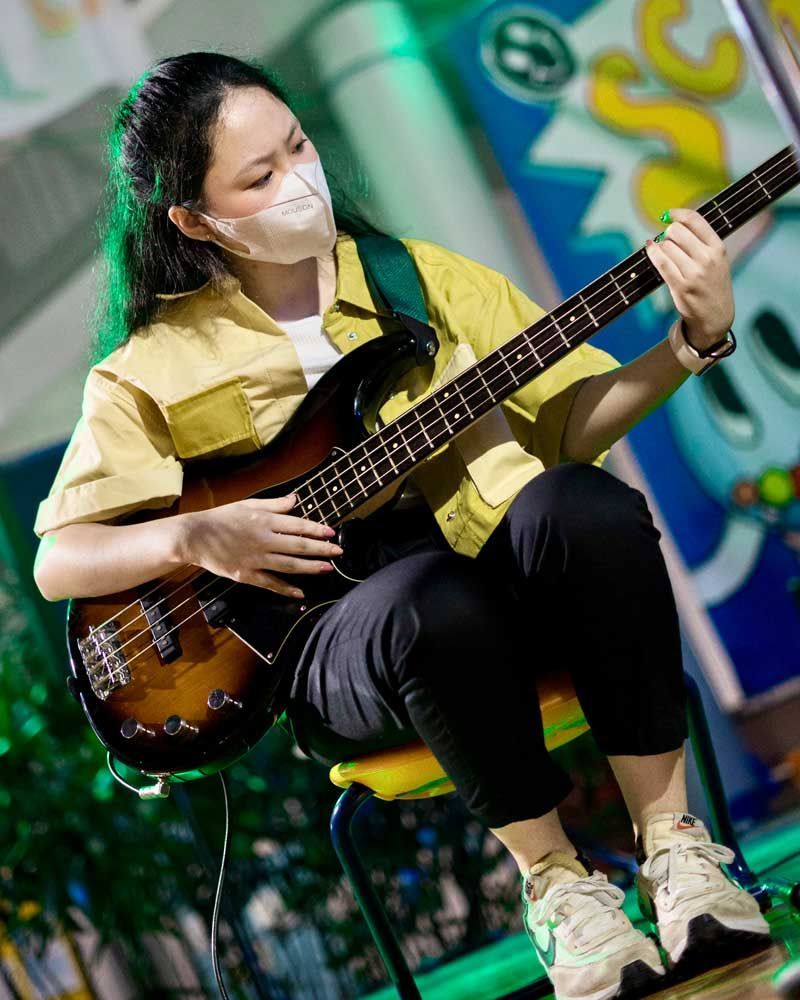 A woman wearing a mask is playing a bass guitar.