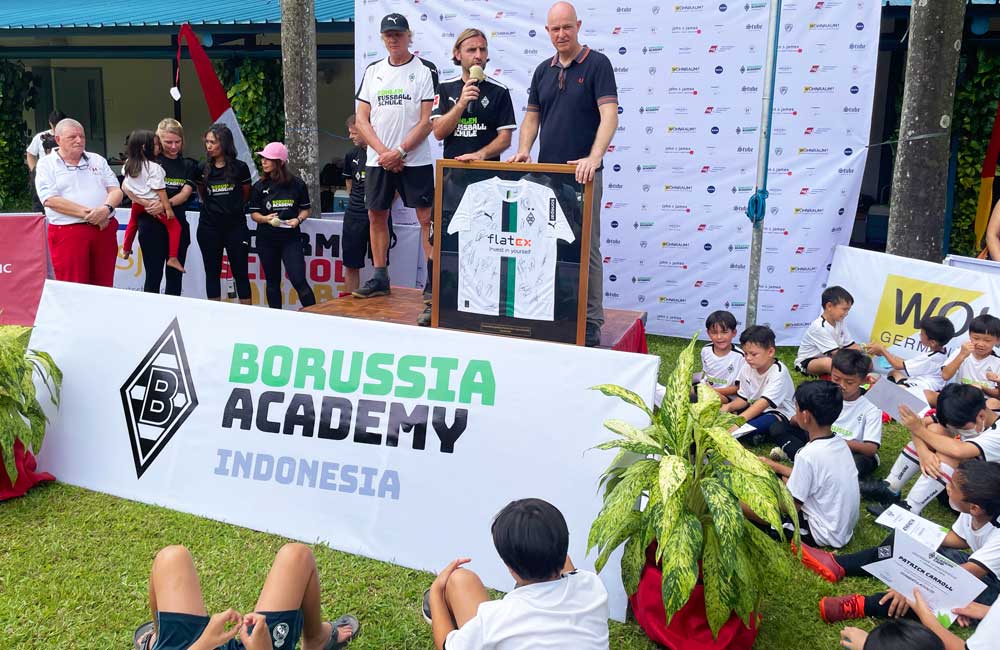 A group of children are sitting in front of a sign that says borussia academy indonesia