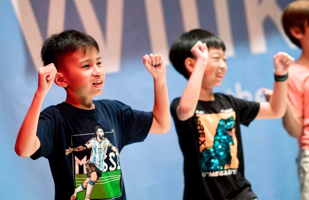 Two young boys are standing next to each other with their hands in the air.