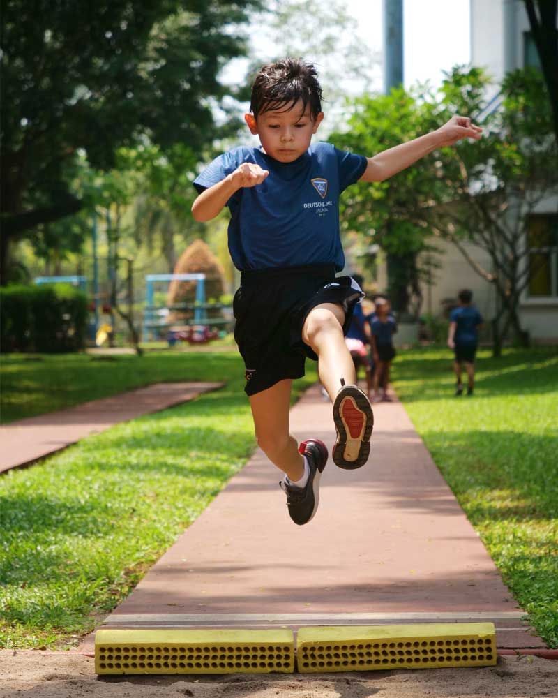 A young boy in a blue shirt is jumping in the air