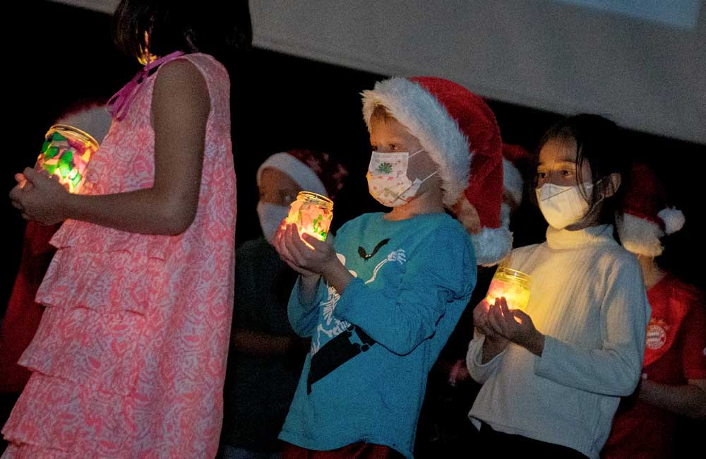 A group of children wearing santa hats and masks are holding candles.