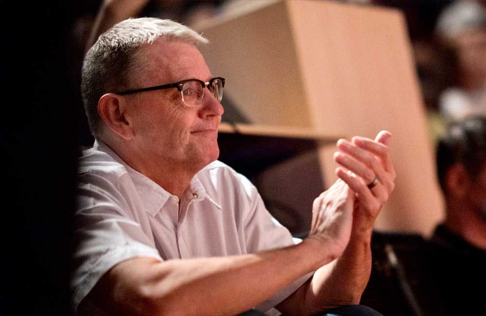 A man wearing glasses is clapping his hands in a dark room.