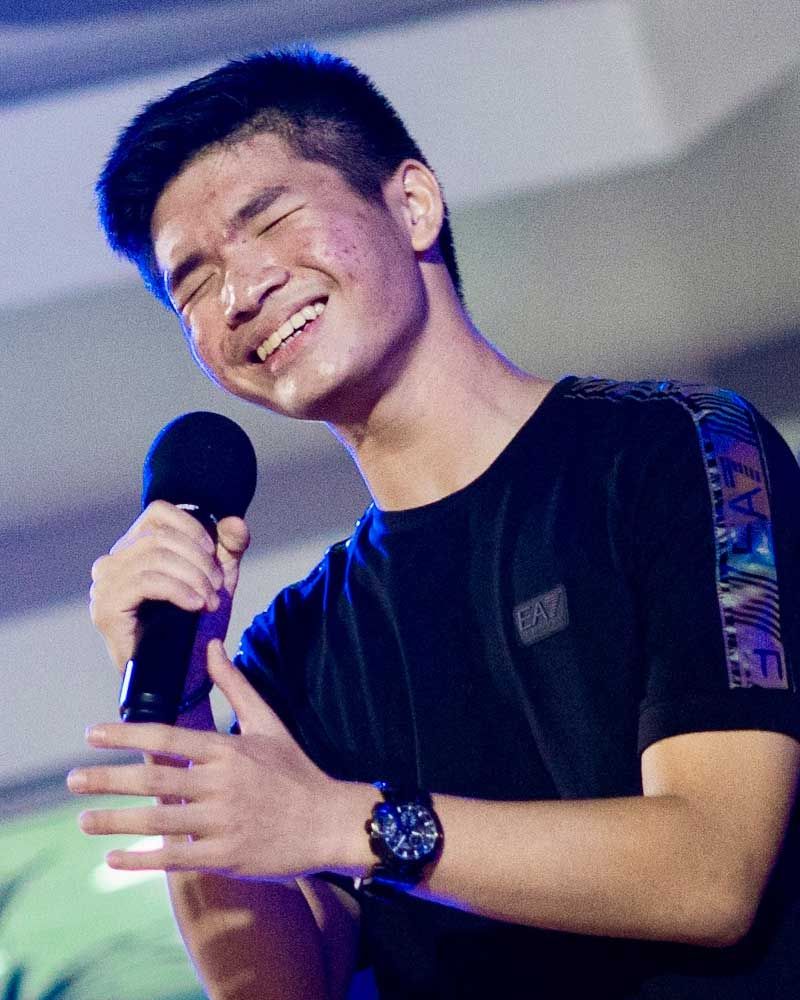 A young man is singing into a microphone and smiling.