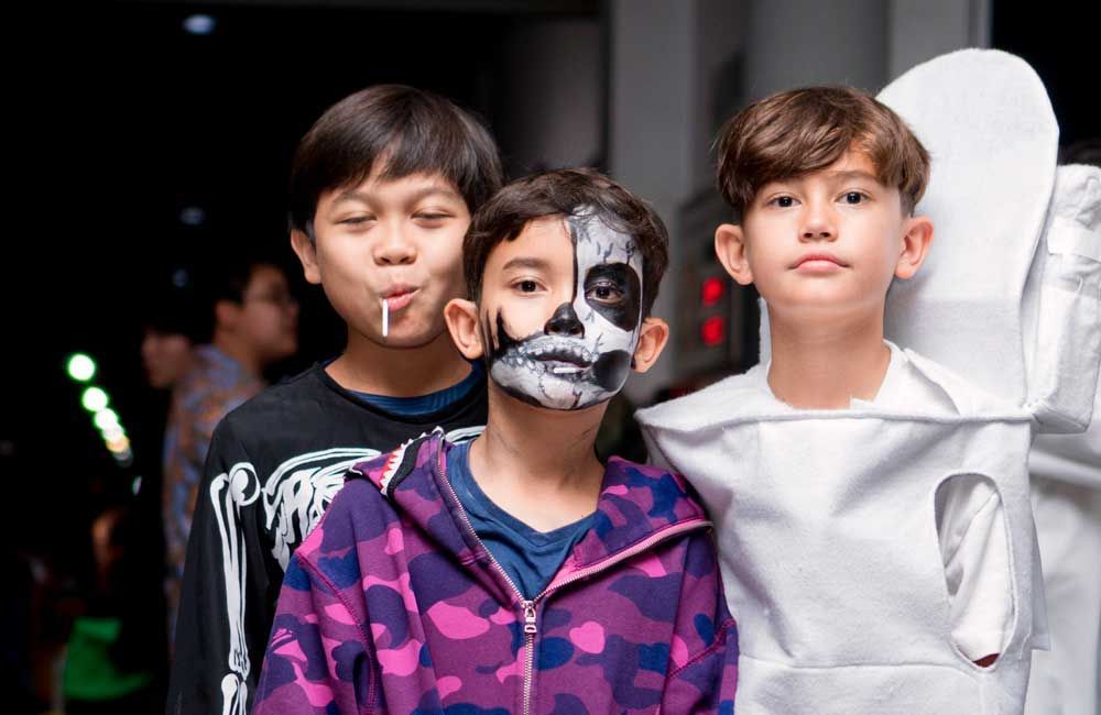 Three young boys are dressed up for halloween and one of them has a skeleton painted on his face.
