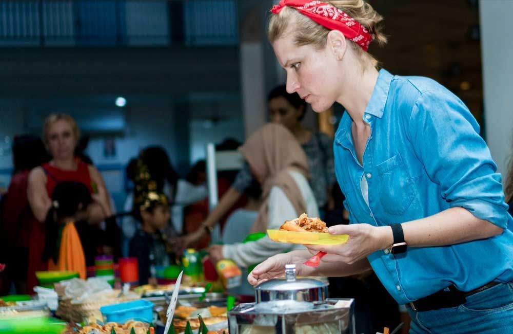 A woman in a blue shirt is serving food at a buffet table.