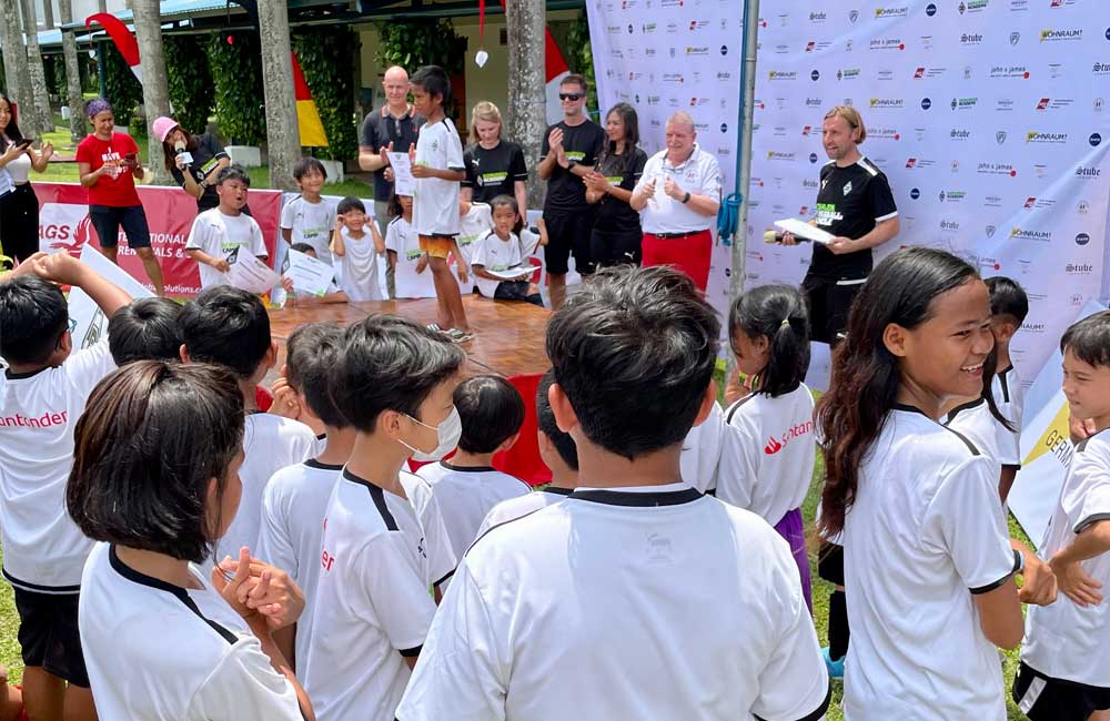 A group of children are standing in front of a group of people.