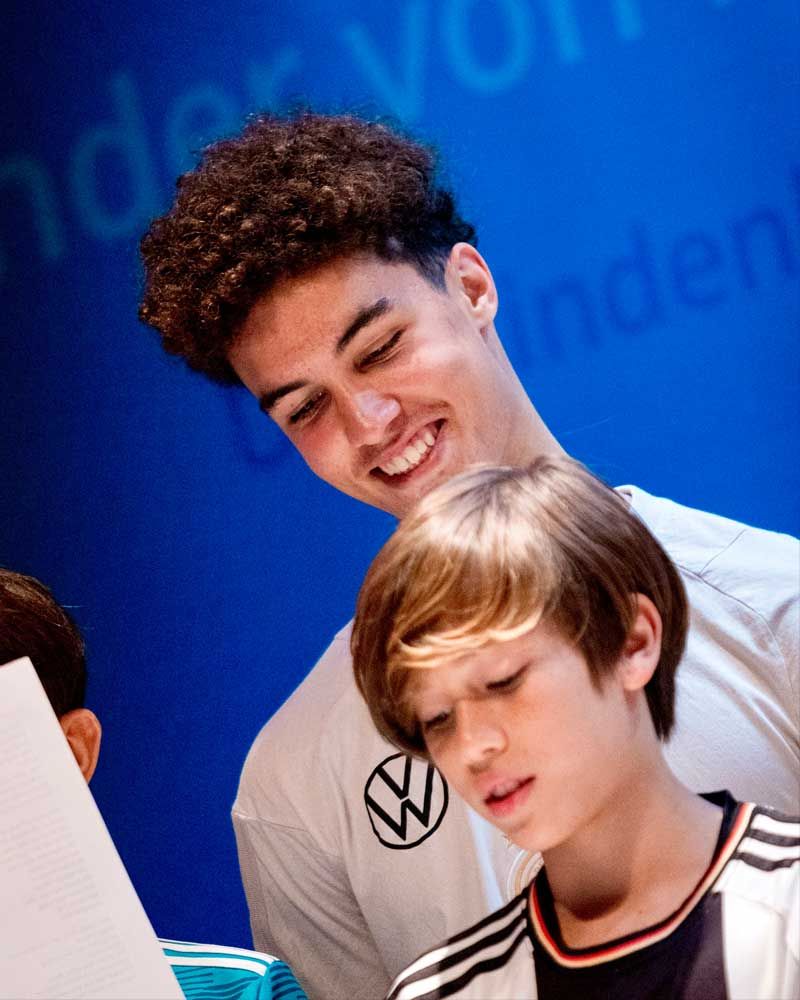A man with a vw logo on his shirt looks at a boy