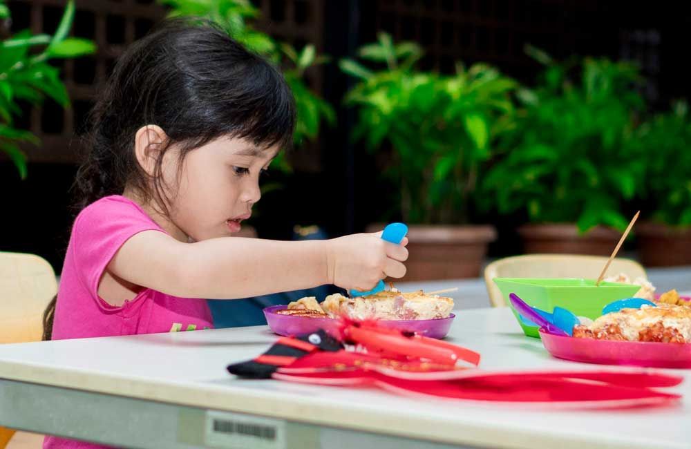 A little girl is sitting at a table playing with food.