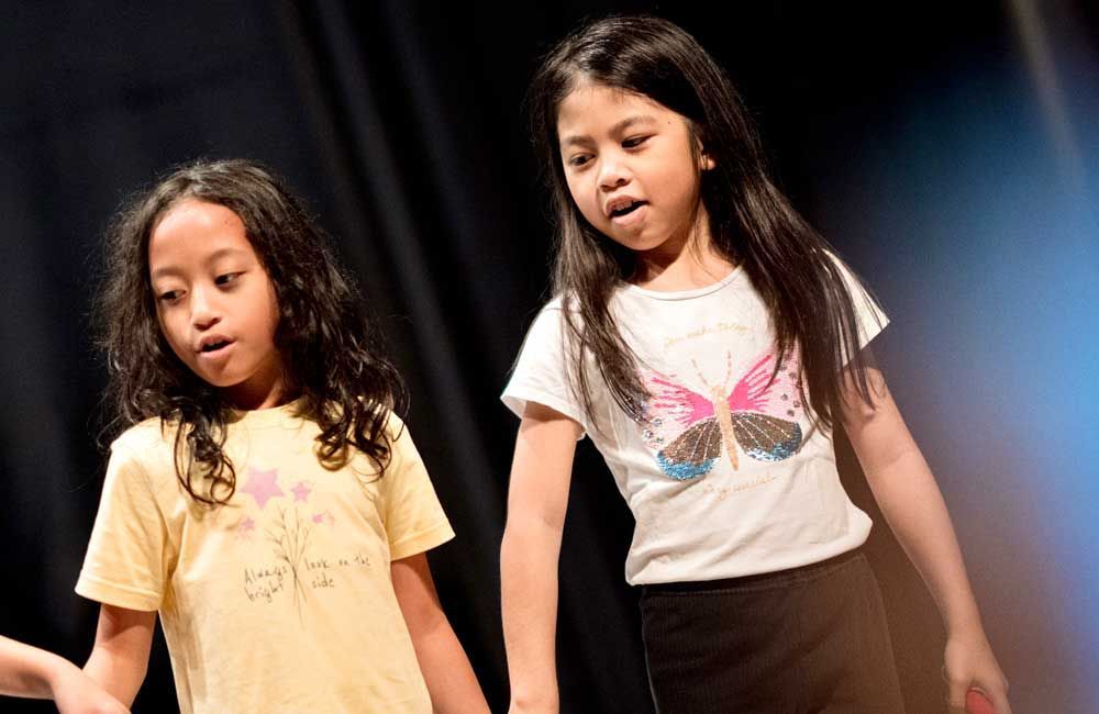 Two young girls are standing next to each other on a stage holding hands.