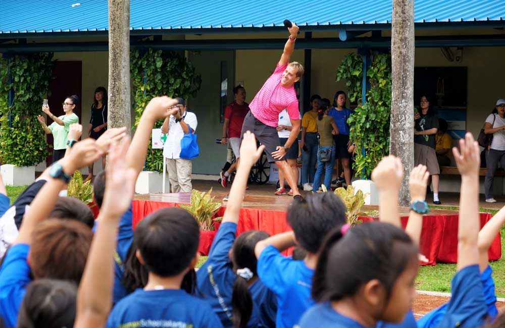 A group of children are raising their hands in the air while a woman stands on a stage.