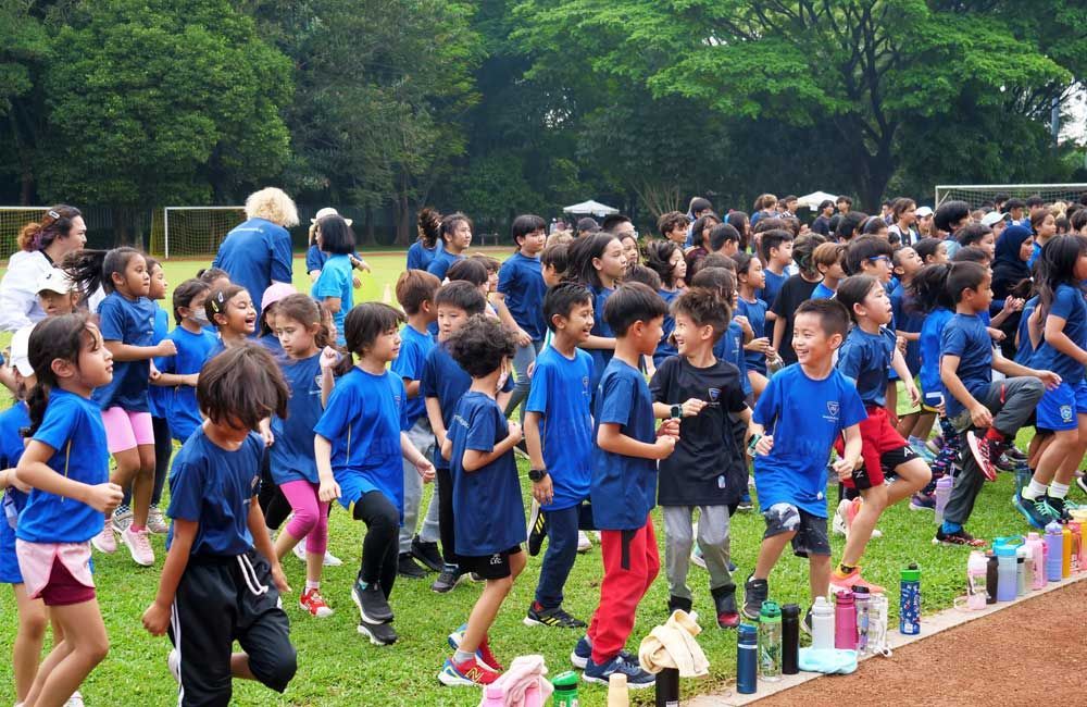 A large group of children in blue shirts are running on a field.