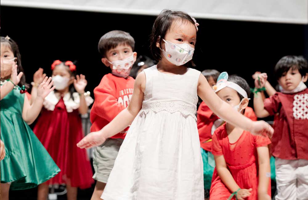 A group of children wearing face masks are dancing on a stage.