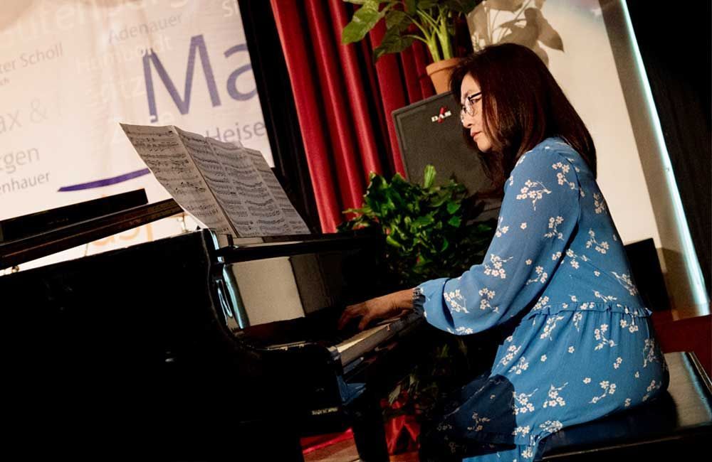 A woman in a blue dress is playing a piano.