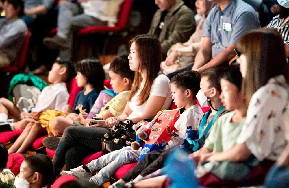 A group of people are sitting in red chairs watching a show.
