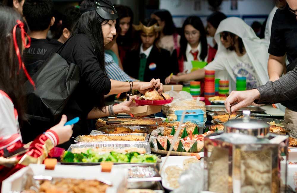 A group of people are standing around a table eating food.