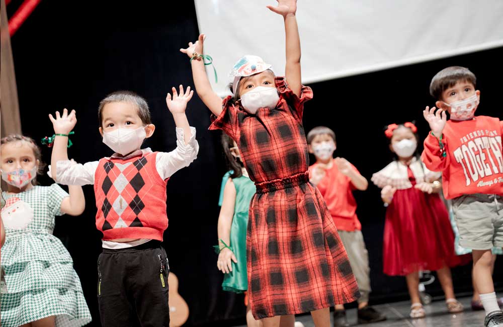 A group of children wearing face masks are dancing on a stage.