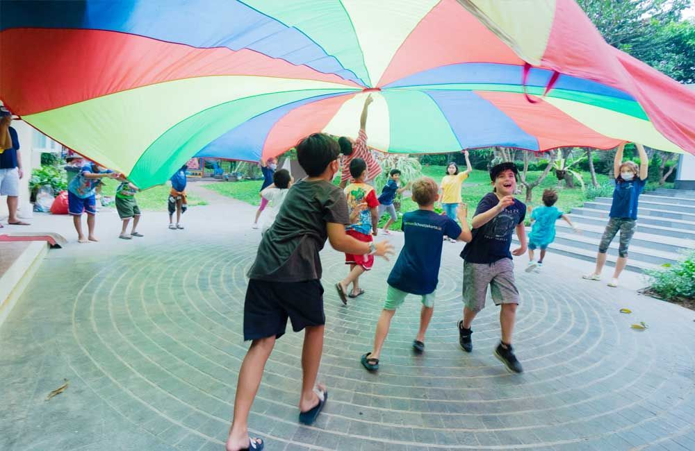A group of children are playing with a colorful parachute.