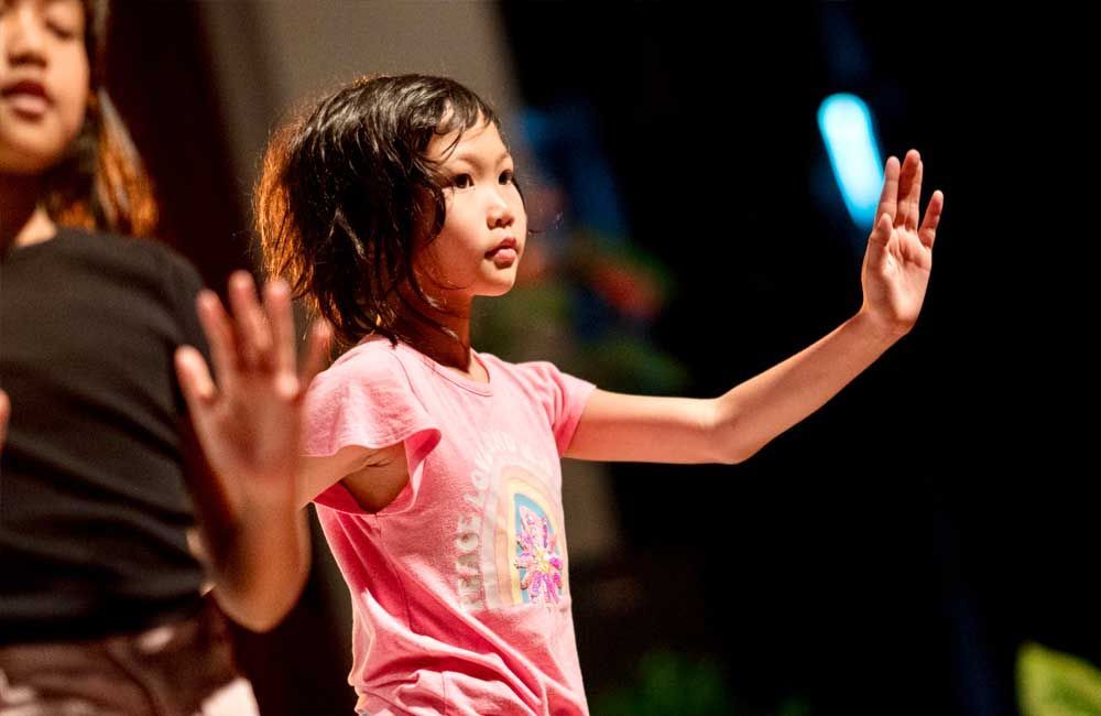A little girl in a pink shirt is dancing on a stage.