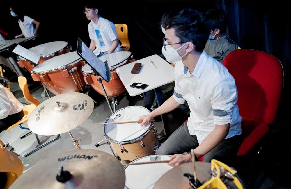 A man wearing a mask is playing drums in a band.