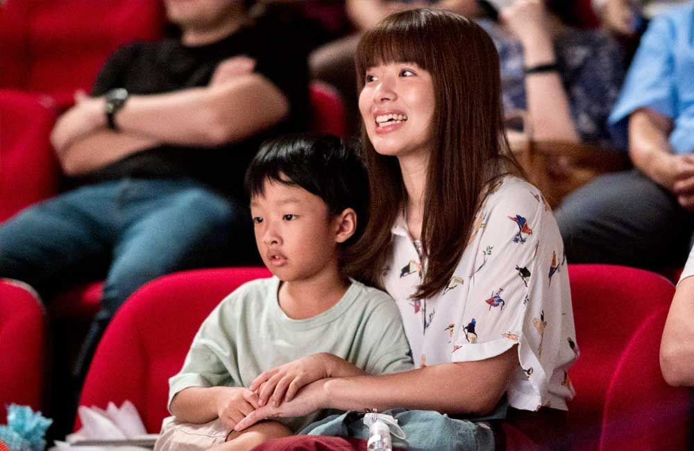 A woman and a child are sitting in a theater watching a movie.