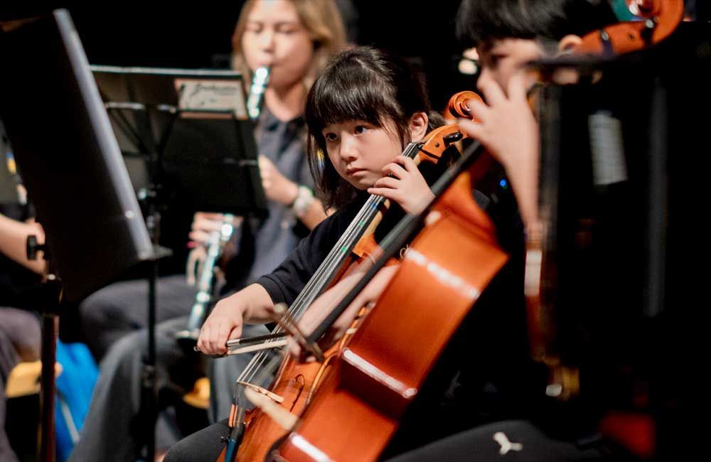 A young girl is playing a cello in an orchestra.