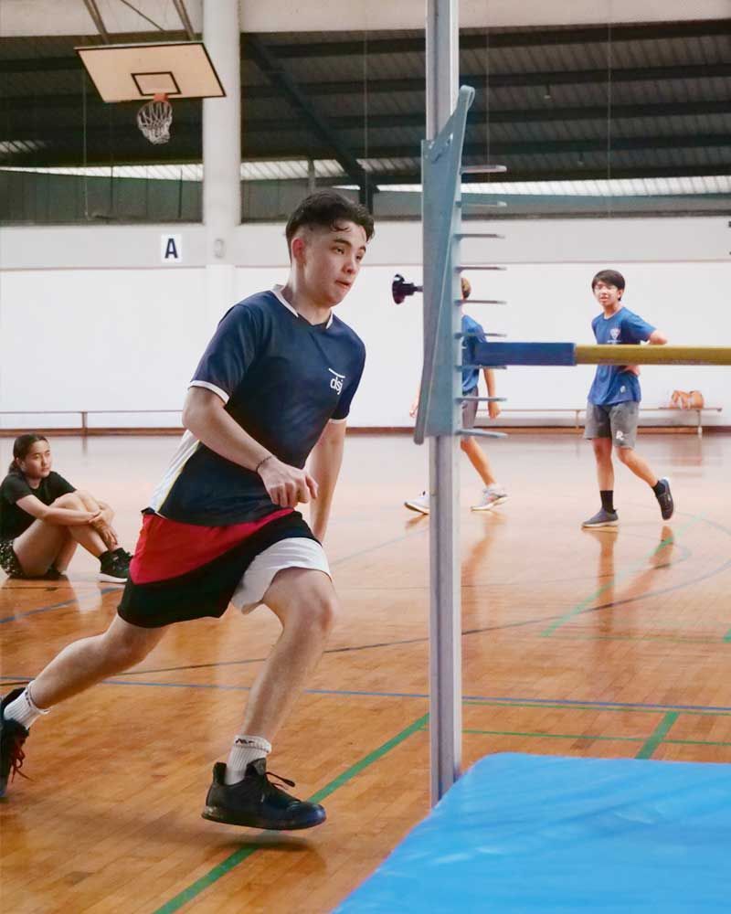 A young boy is jumping over a pole in a gym.
