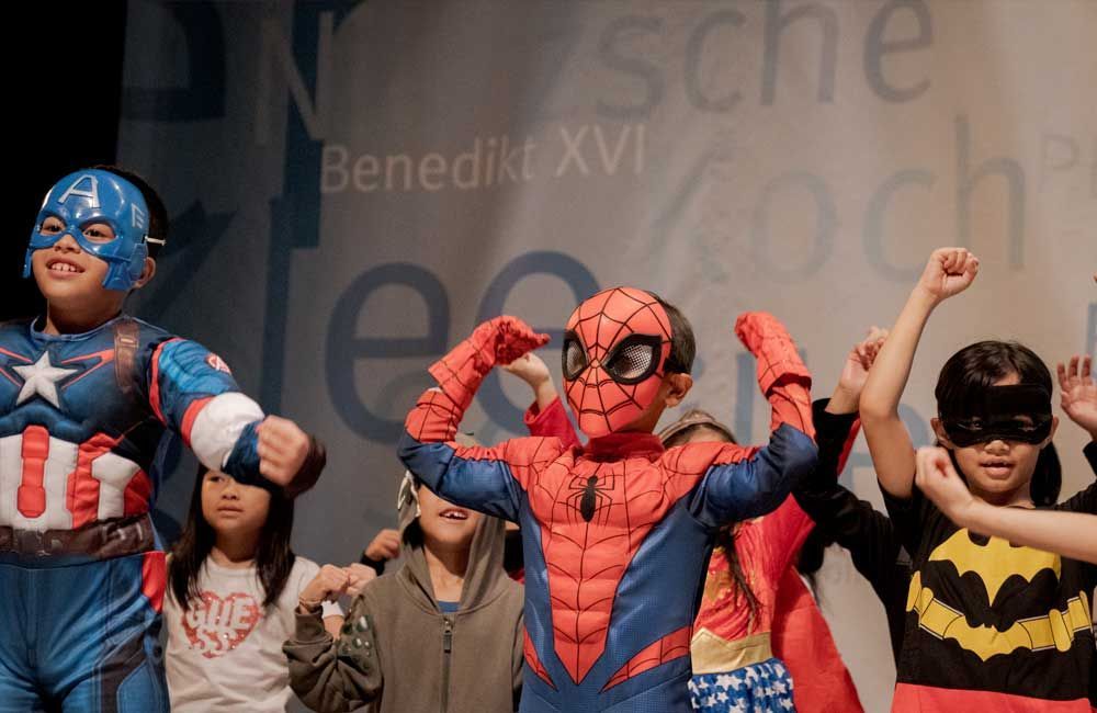 A group of children dressed in superhero costumes are dancing on a stage.