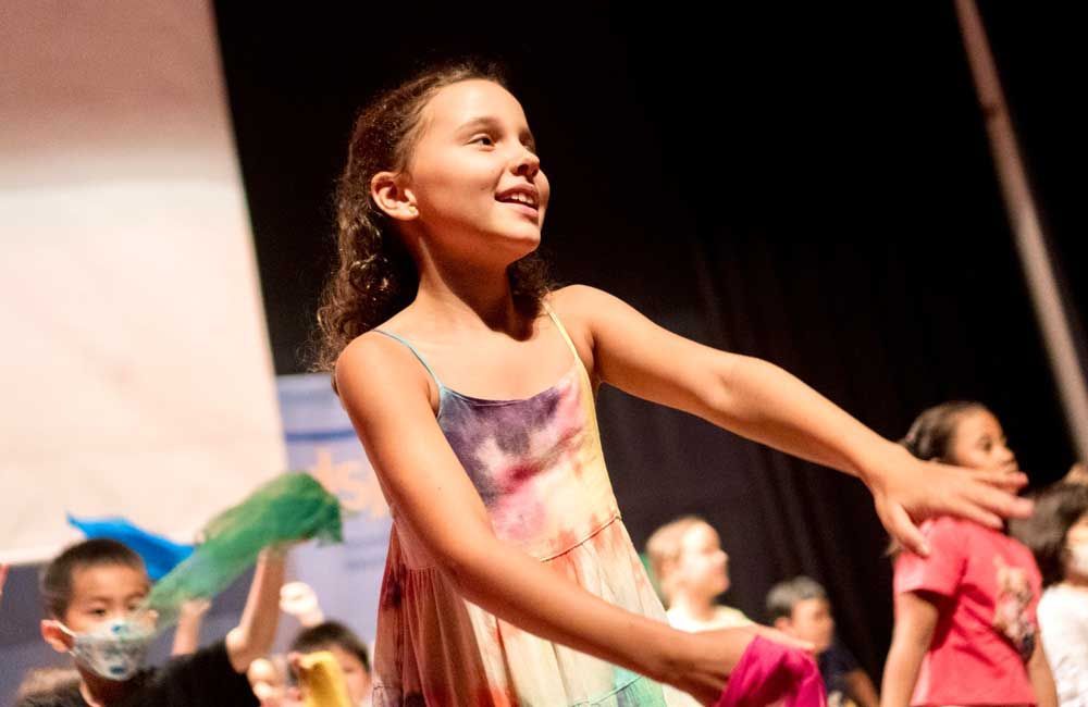 A young girl is dancing on a stage with other children.