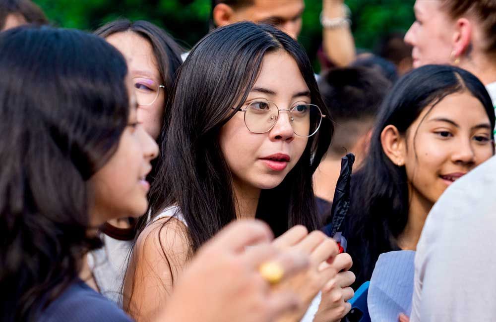 A woman wearing glasses is standing in a crowd of people.