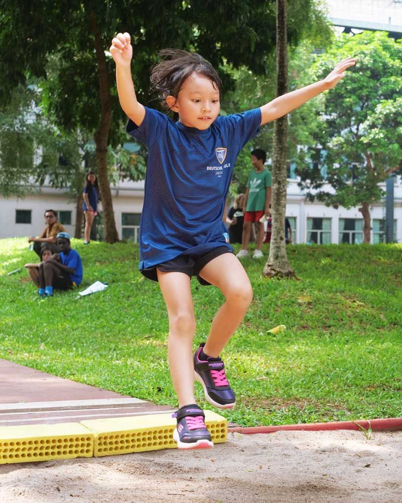 A little girl in a blue shirt is jumping in the air