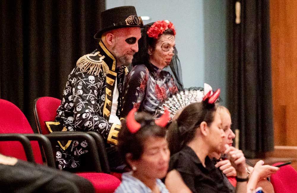 A group of people dressed in costumes are sitting in red chairs.