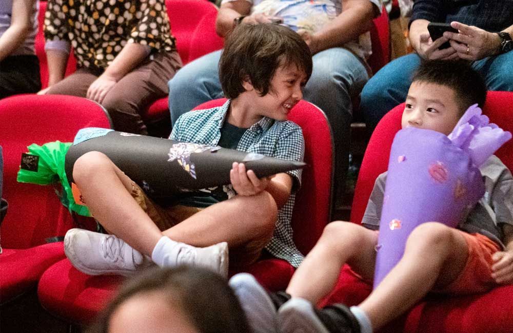 A group of children are sitting in red chairs in a theater.