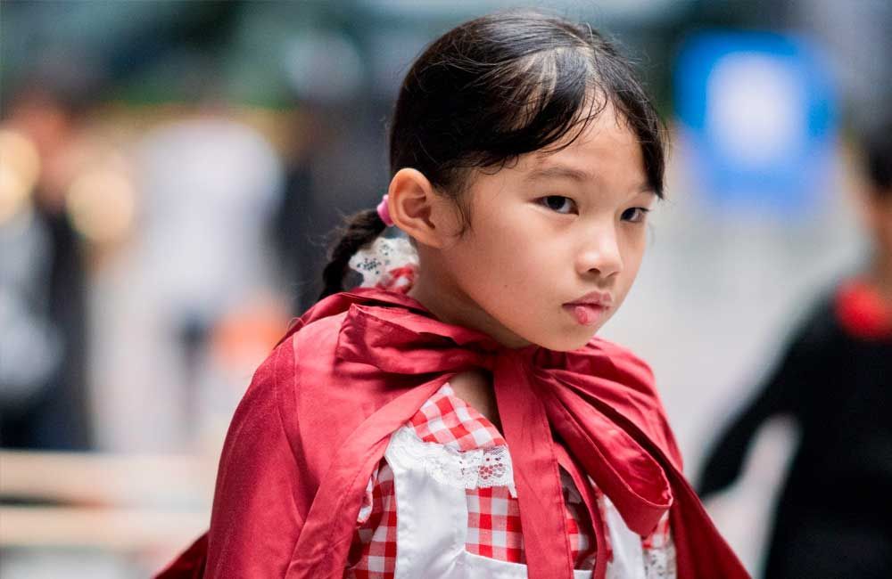 A little girl is wearing a red cape and looking at the camera.