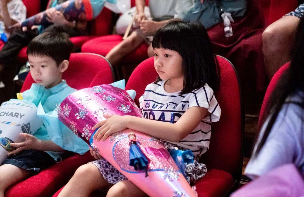 A boy and a girl are sitting in red chairs holding balloons.