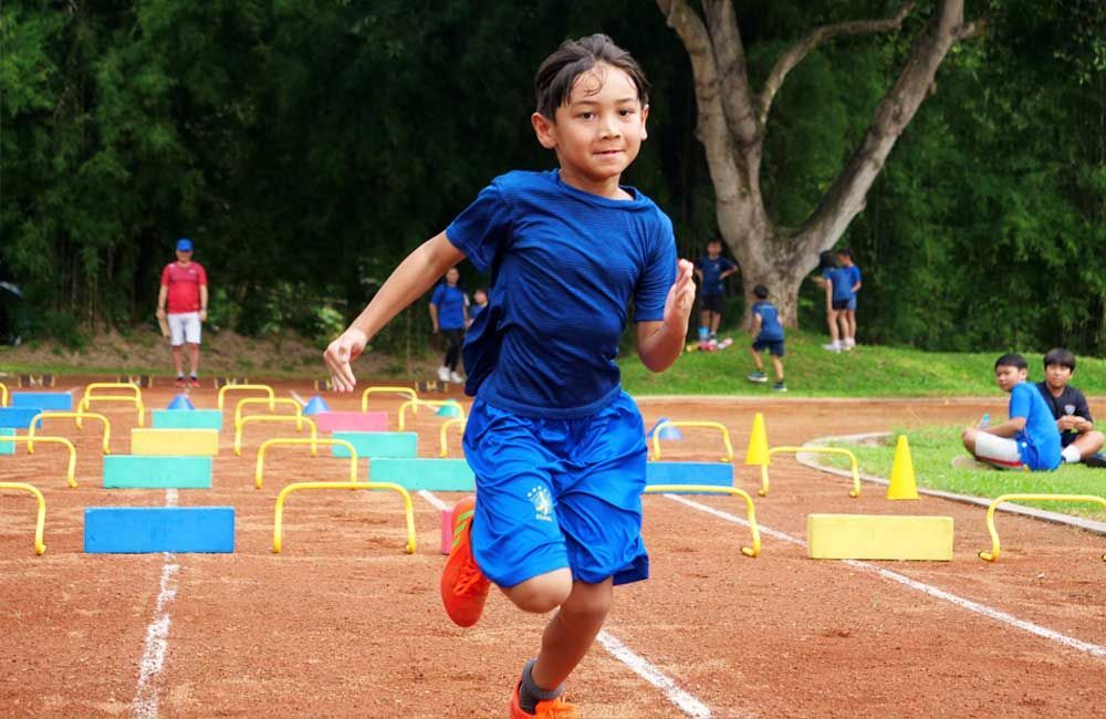 A young boy is running on a track with hurdles.