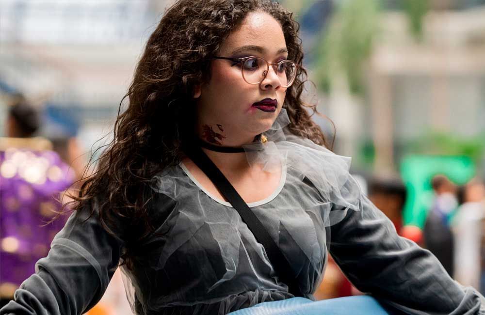 A woman with curly hair is wearing glasses and a choker.